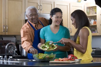 Family making a salad together. Mom is serving the daughter and the father is stealing a vegetable from the bowl.