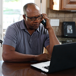 Man sitting at kitchen table working on laptop computer.